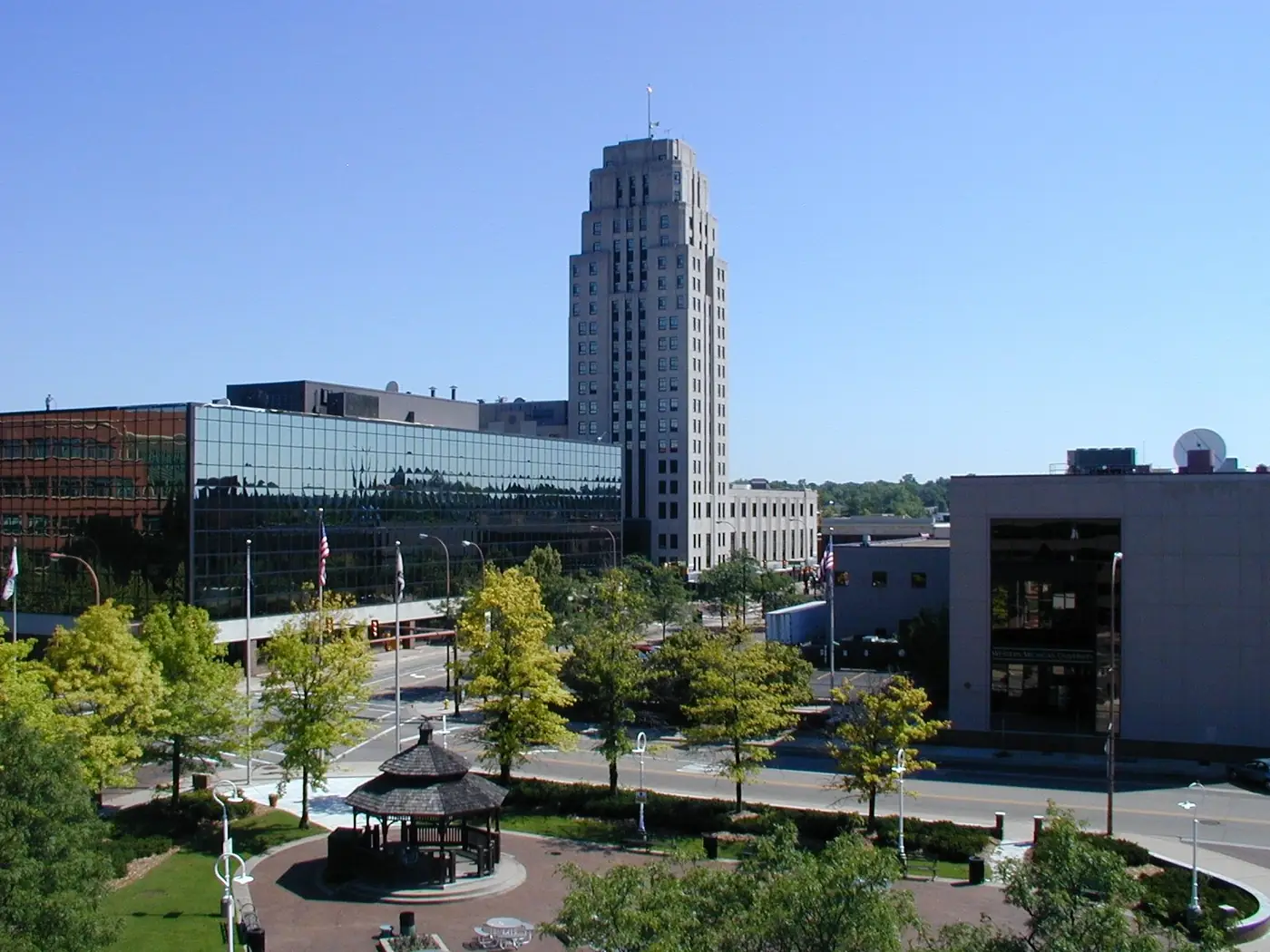Downtown Battle Creek on a sunny day, with a tall Art Deco tower, a glass office building and a park gazebo among trees